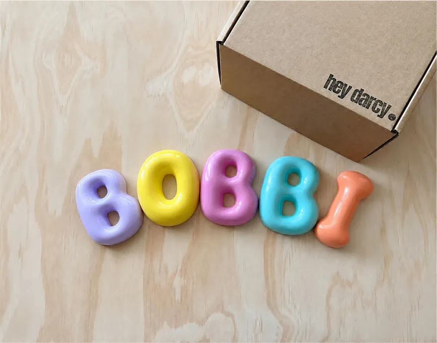 Personalised bubble letters spelling BOBBI in pastel colours, beside a Hey Darcy box